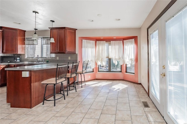 kitchen with decorative light fixtures, visible vents, backsplash, black microwave, and a kitchen bar