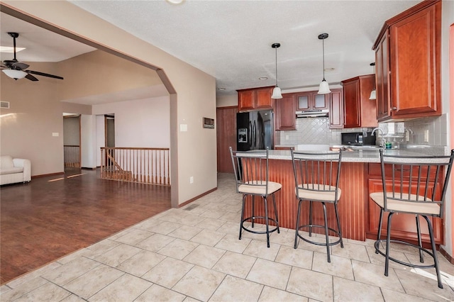 kitchen with arched walkways, light countertops, black refrigerator with ice dispenser, a peninsula, and under cabinet range hood