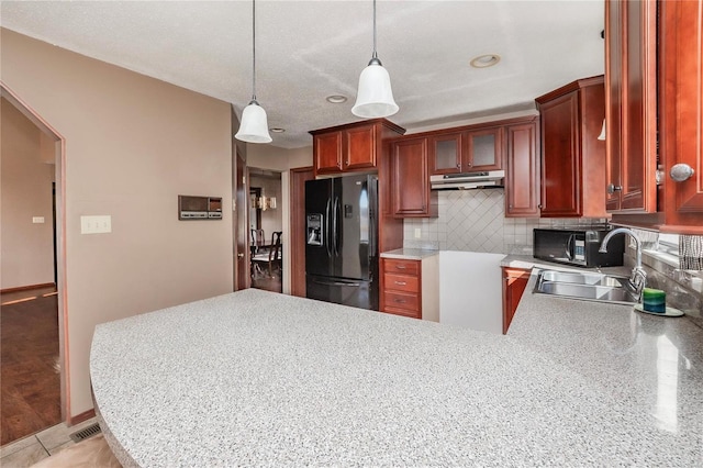 kitchen featuring under cabinet range hood, a peninsula, a sink, backsplash, and black appliances