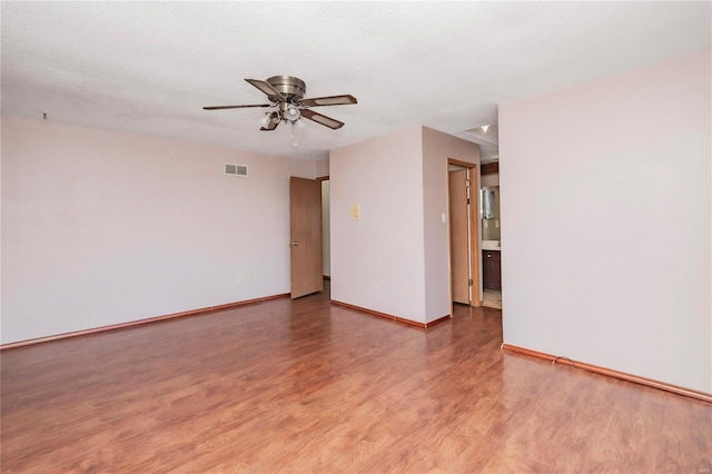 empty room with a textured ceiling, wood finished floors, a ceiling fan, visible vents, and baseboards