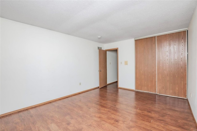 unfurnished bedroom featuring a closet, a textured ceiling, baseboards, and wood finished floors