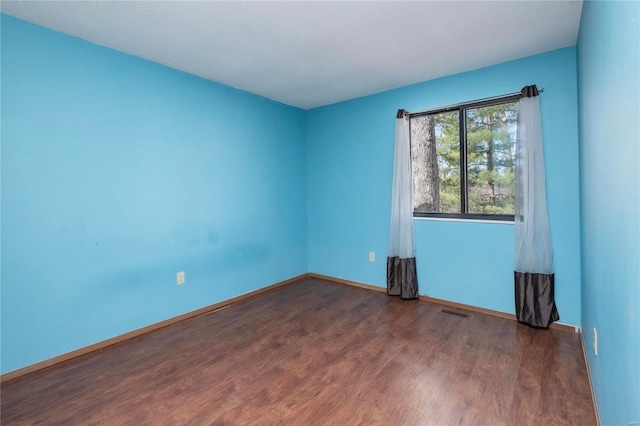 empty room featuring wood finished floors, visible vents, and baseboards