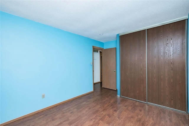 unfurnished bedroom with a textured ceiling, a closet, baseboards, and wood finished floors