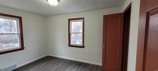 unfurnished bedroom featuring baseboards, multiple windows, visible vents, and dark wood finished floors