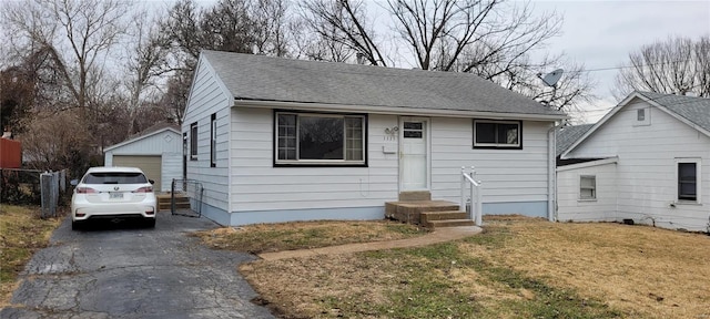 view of front facade with an outbuilding, roof with shingles, a garage, driveway, and a front lawn