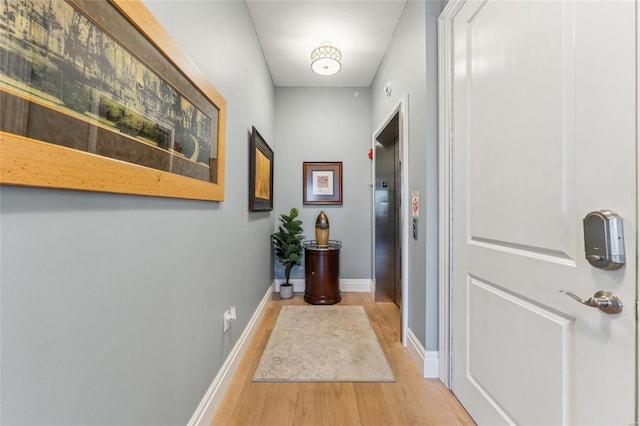 hall with baseboards, elevator, and light wood-style flooring