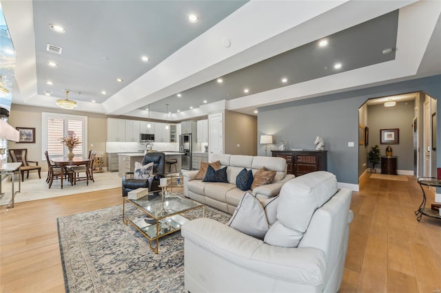 living room featuring visible vents, recessed lighting, a raised ceiling, and light wood-style floors