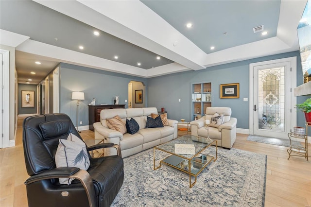 living area with a tray ceiling, arched walkways, visible vents, and light wood finished floors