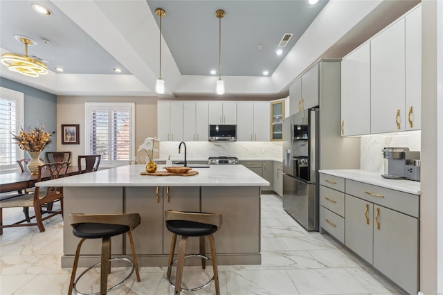 kitchen with a tray ceiling, gray cabinets, stainless steel microwave, fridge with ice dispenser, and marble finish floor