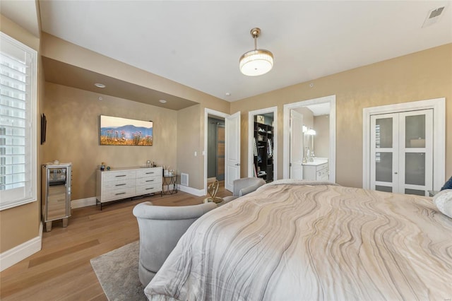 bedroom featuring visible vents, wood finished floors, baseboards, and ensuite bathroom