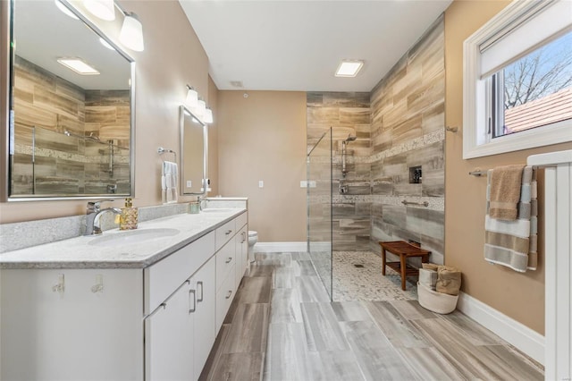 full bathroom with double vanity, tiled shower, baseboards, and a sink