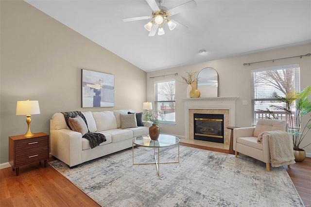 living area with baseboards, a ceiling fan, lofted ceiling, wood finished floors, and a high end fireplace