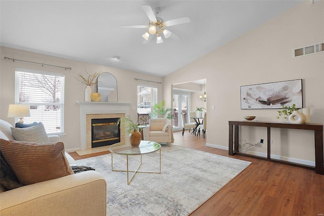 living area featuring a premium fireplace, wood finished floors, visible vents, baseboards, and a ceiling fan