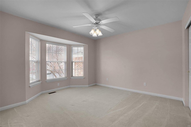 empty room with a ceiling fan, light colored carpet, visible vents, and baseboards