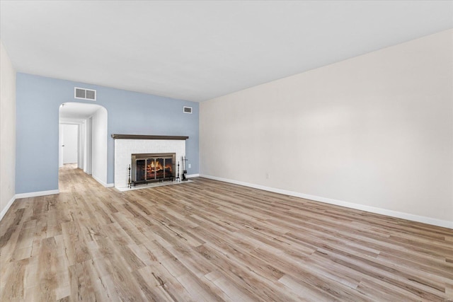 unfurnished living room featuring visible vents, baseboards, light wood-type flooring, and a fireplace with flush hearth