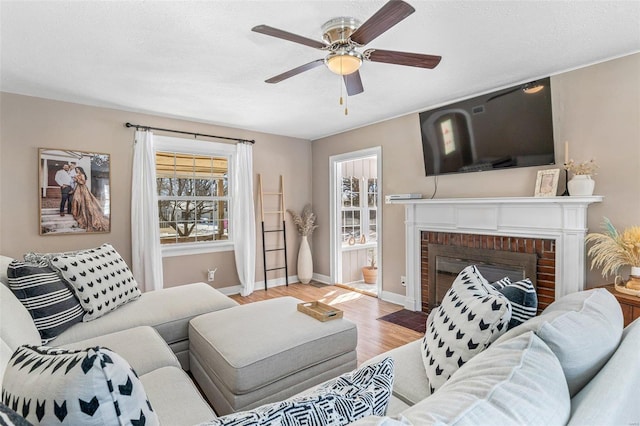 living room with baseboards, a ceiling fan, a textured ceiling, light wood-type flooring, and a fireplace