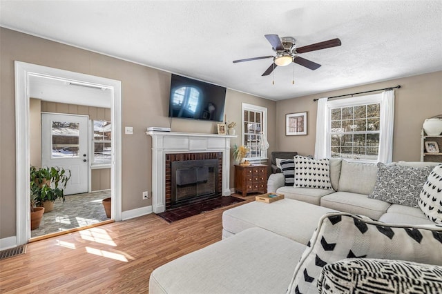 living room with visible vents, ceiling fan, wood finished floors, a textured ceiling, and a brick fireplace