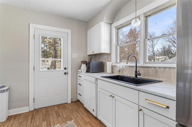 kitchen featuring dishwasher, light wood-style flooring, light stone counters, white cabinetry, and a sink