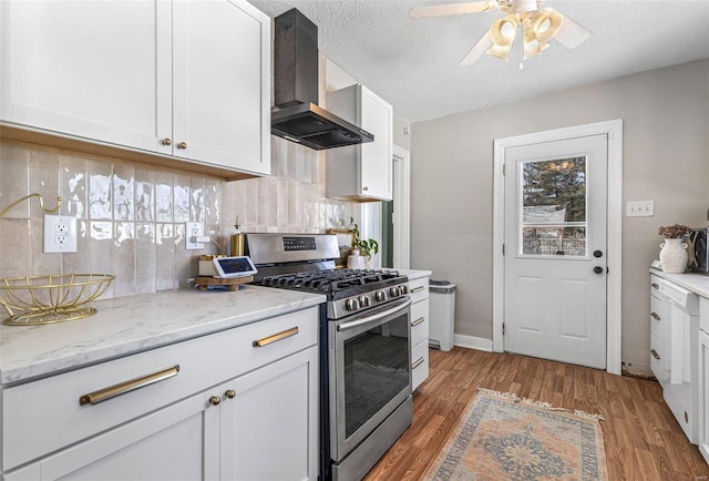 kitchen with stainless steel gas range oven, light stone counters, white cabinets, light wood-type flooring, and wall chimney exhaust hood