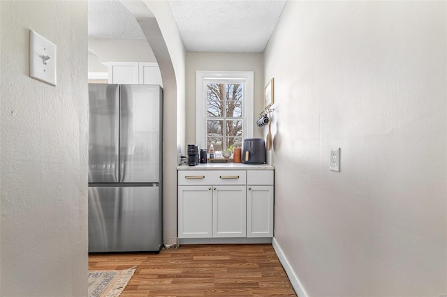 kitchen with light wood-type flooring, white cabinetry, light countertops, and freestanding refrigerator