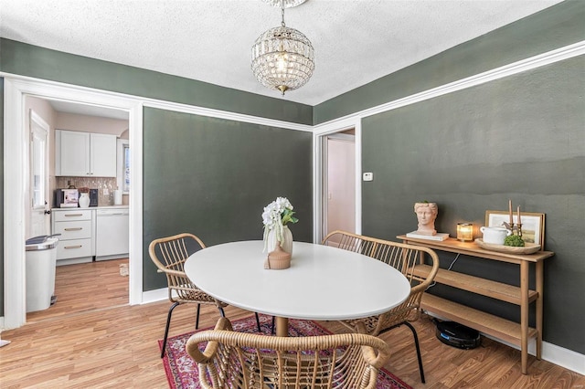 dining area with light wood-type flooring, a textured ceiling, baseboards, and a notable chandelier