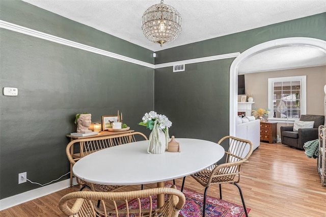 dining area with arched walkways, a fireplace, visible vents, wood finished floors, and a chandelier