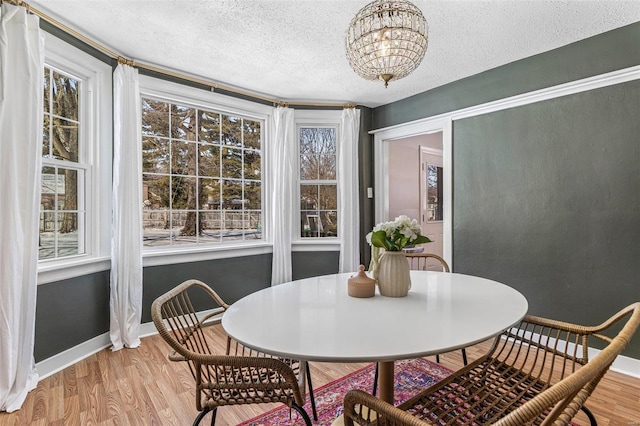 dining area with a chandelier, a textured ceiling, baseboards, and wood finished floors