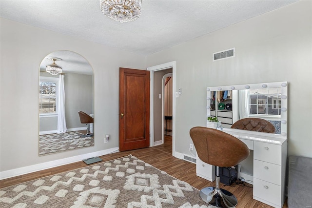 office space with baseboards, visible vents, arched walkways, wood finished floors, and a textured ceiling