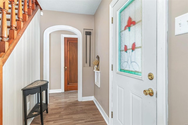 foyer with arched walkways, wood finished floors, stairs, and baseboards