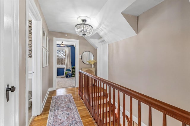 hall with light wood-type flooring, an inviting chandelier, and baseboards