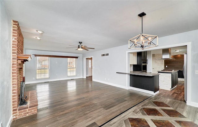 kitchen featuring baseboards, visible vents, dark wood-style flooring, a peninsula, and ceiling fan with notable chandelier