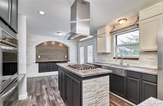 kitchen with a sink, a kitchen island, appliances with stainless steel finishes, tasteful backsplash, and island exhaust hood