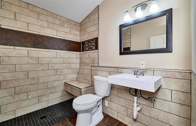 full bath with a wainscoted wall, tile walls, toilet, a tile shower, and a sink