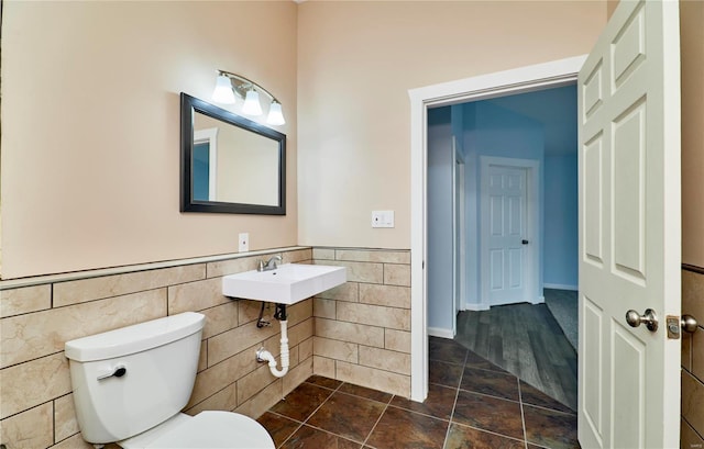 bathroom featuring toilet, wainscoting, a sink, and tile walls