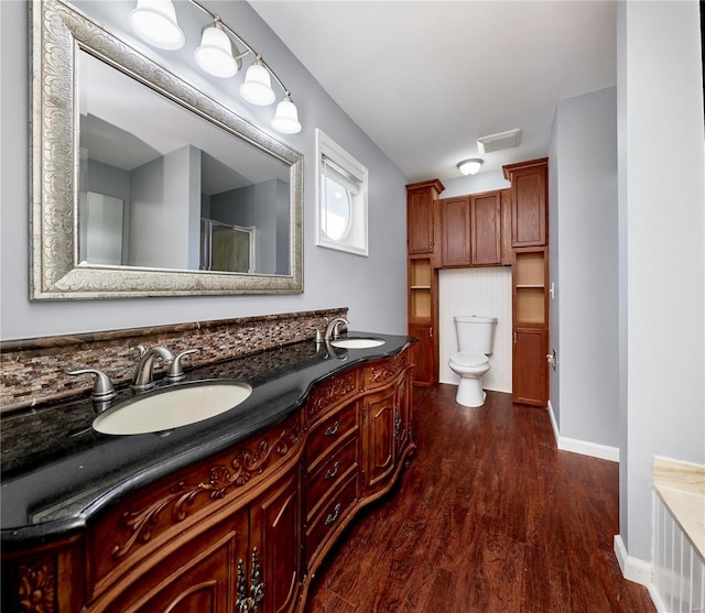 bathroom featuring double vanity, toilet, wood finished floors, an enclosed shower, and a sink