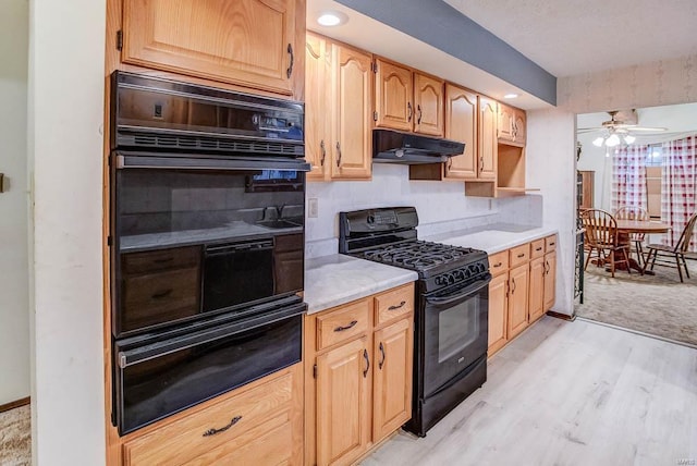 kitchen with light wood-style floors, under cabinet range hood, light countertops, black appliances, and a warming drawer