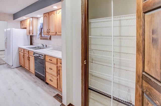 kitchen with a sink, black dishwasher, light countertops, freestanding refrigerator, and light wood finished floors