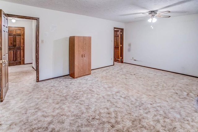 unfurnished room with ceiling fan, baseboards, a textured ceiling, and light colored carpet