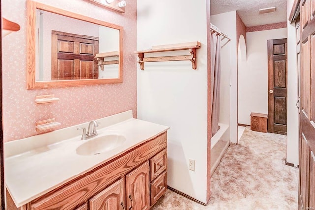 full bathroom with a shower with curtain, a textured ceiling, vanity, and wallpapered walls