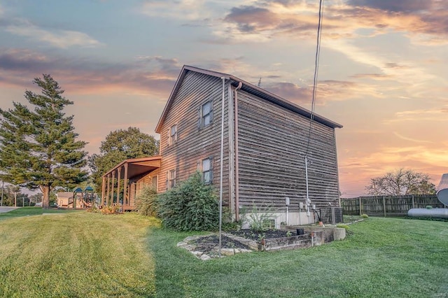 property exterior at dusk featuring a vegetable garden, a lawn, and fence