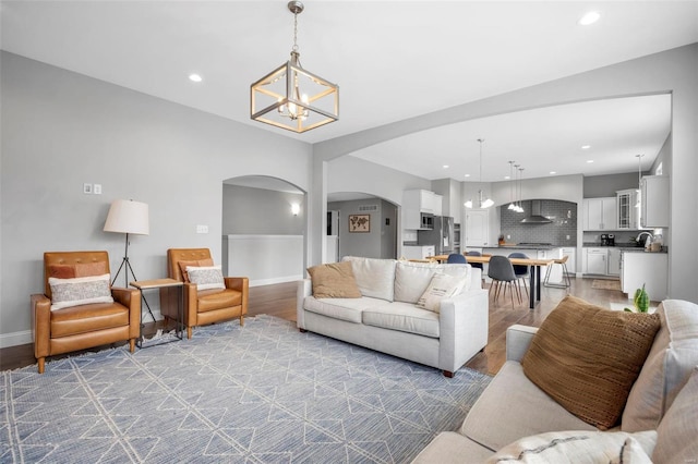 living area with baseboards, light wood finished floors, recessed lighting, arched walkways, and a chandelier