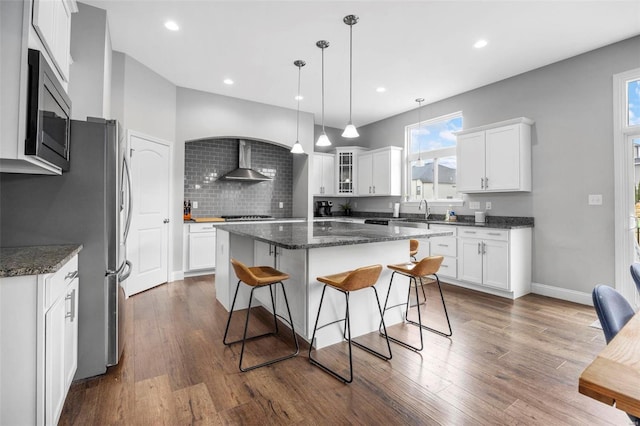 kitchen with a breakfast bar, dark wood-style flooring, stainless steel microwave, wall chimney exhaust hood, and a center island