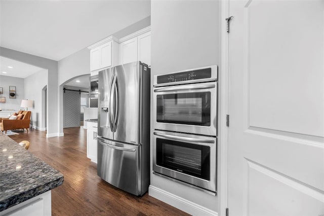 kitchen featuring dark stone countertops, dark wood-style floors, arched walkways, stainless steel appliances, and white cabinetry