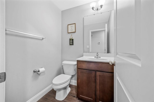 half bath featuring baseboards, toilet, wood finished floors, and vanity