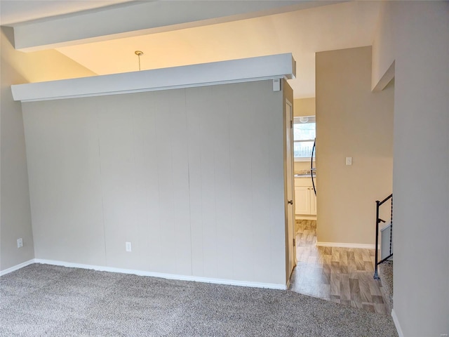 empty room with baseboards, beamed ceiling, and light colored carpet