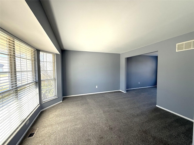 empty room featuring dark colored carpet, visible vents, lofted ceiling, and baseboards