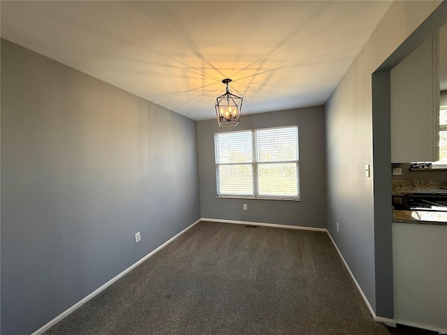 unfurnished dining area featuring dark colored carpet, a notable chandelier, and baseboards