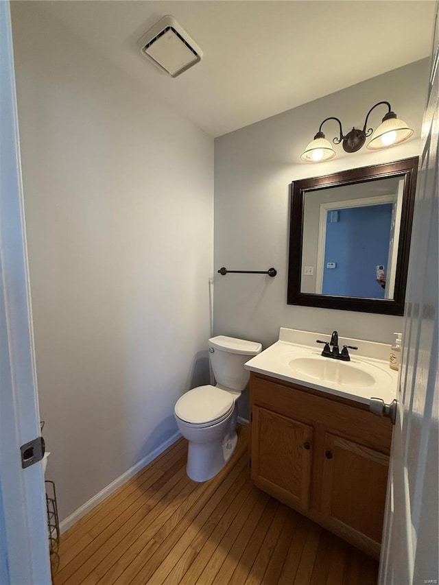 half bath featuring toilet, wood-type flooring, baseboards, and vanity