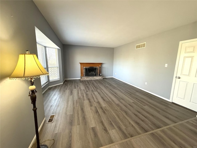 unfurnished living room featuring a brick fireplace, wood finished floors, visible vents, and baseboards