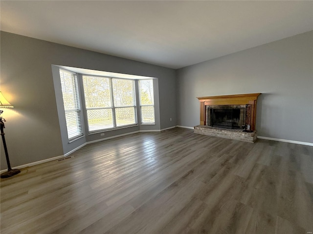 unfurnished living room featuring a brick fireplace, visible vents, baseboards, and wood finished floors